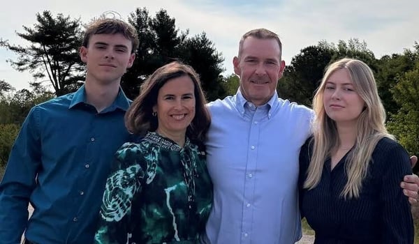 Natalie and her family smiling together outdoors in front of tall trees