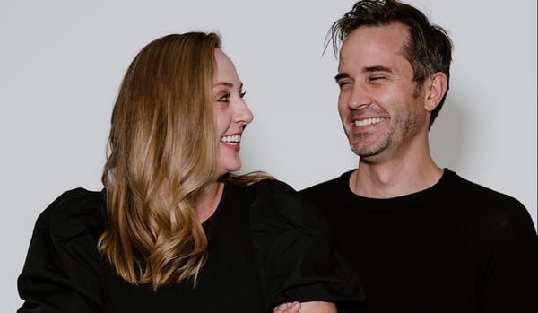 Paul and Miranda smiling at each other against a white backdrop