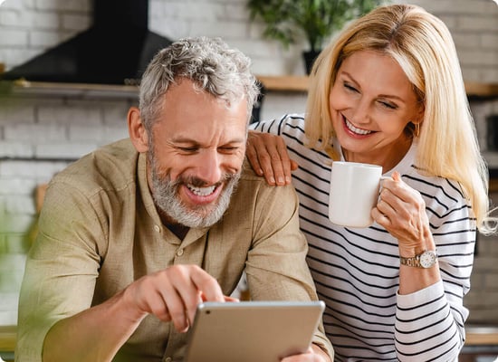 Smiling older couple looks at a tablet together in their kitchen