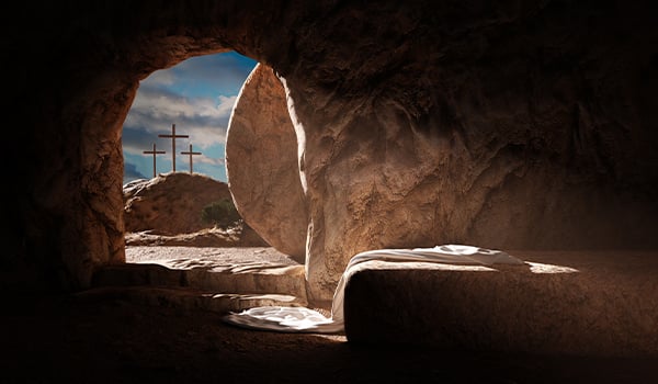 View from inside an empty tomb, its stone rolled away, with linen cloths and three crosses on a distant hill