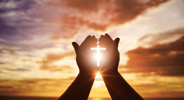 Hands holding an illuminated cross.
