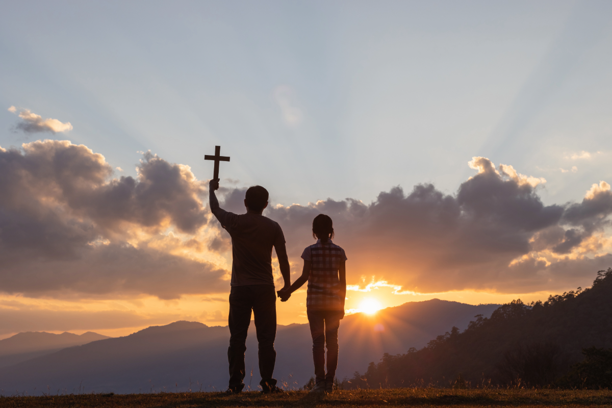 Silhouette of man holding woman's hand with a cross in the other hand