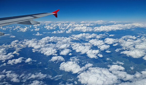 View from an airplane window of the wing over white clouds and mountains far below