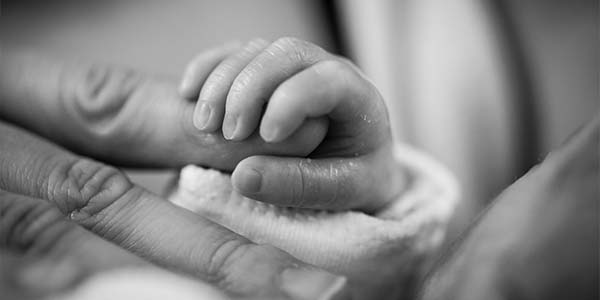 Black-and-white close-up of a baby's tiny hand gripping an adult's finger