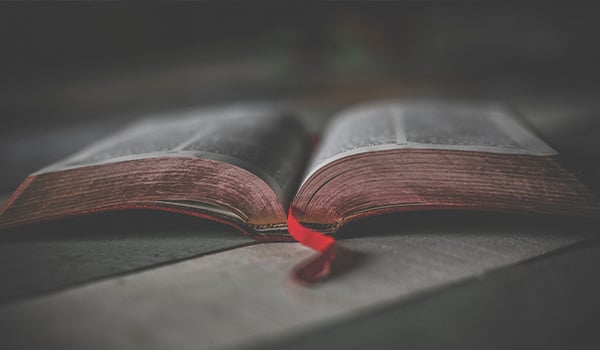 Open Bible with a red ribbon bookmark resting on a wooden table