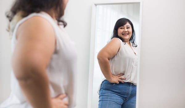 Smiling woman with hands on her hips looking at her reflection in a full-length mirror