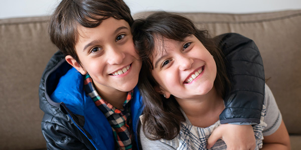 Smiling boy and girl hugging cheek to cheek on a couch
