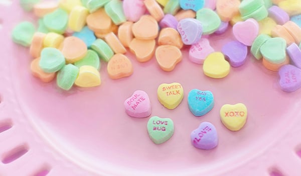 Pastel candy conversation hearts with messages like Sweet Talk and Love Bug on a pink plate