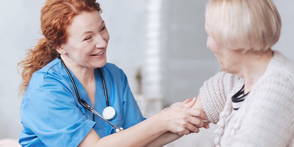 Smiling nurse in blue scrubs holding the hands of an older woman