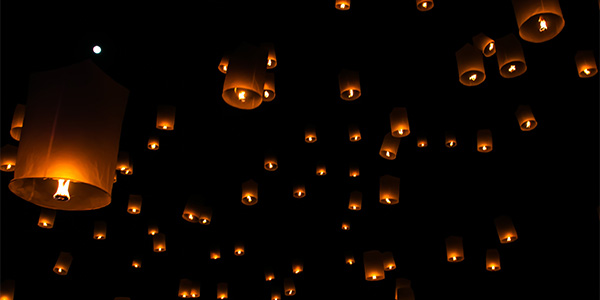 Dozens of glowing paper sky lanterns floating into a black night sky