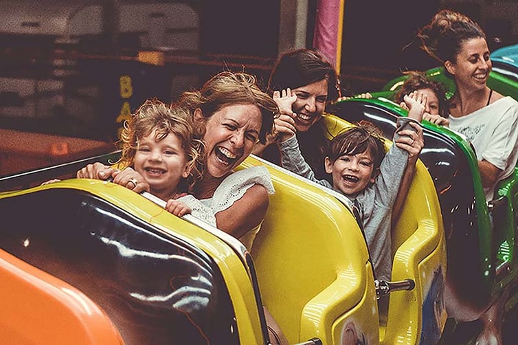 Moms and toddlers laughing on a kiddie roller coaster