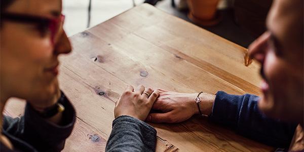 couple sitting at table with hands placed on top of each other