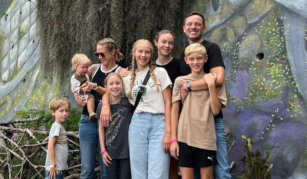Two adults and six children smile together in front of a colorful painted mural
