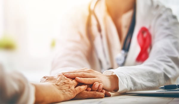 Doctor in a white coat and stethoscope holding an older patient’s hand