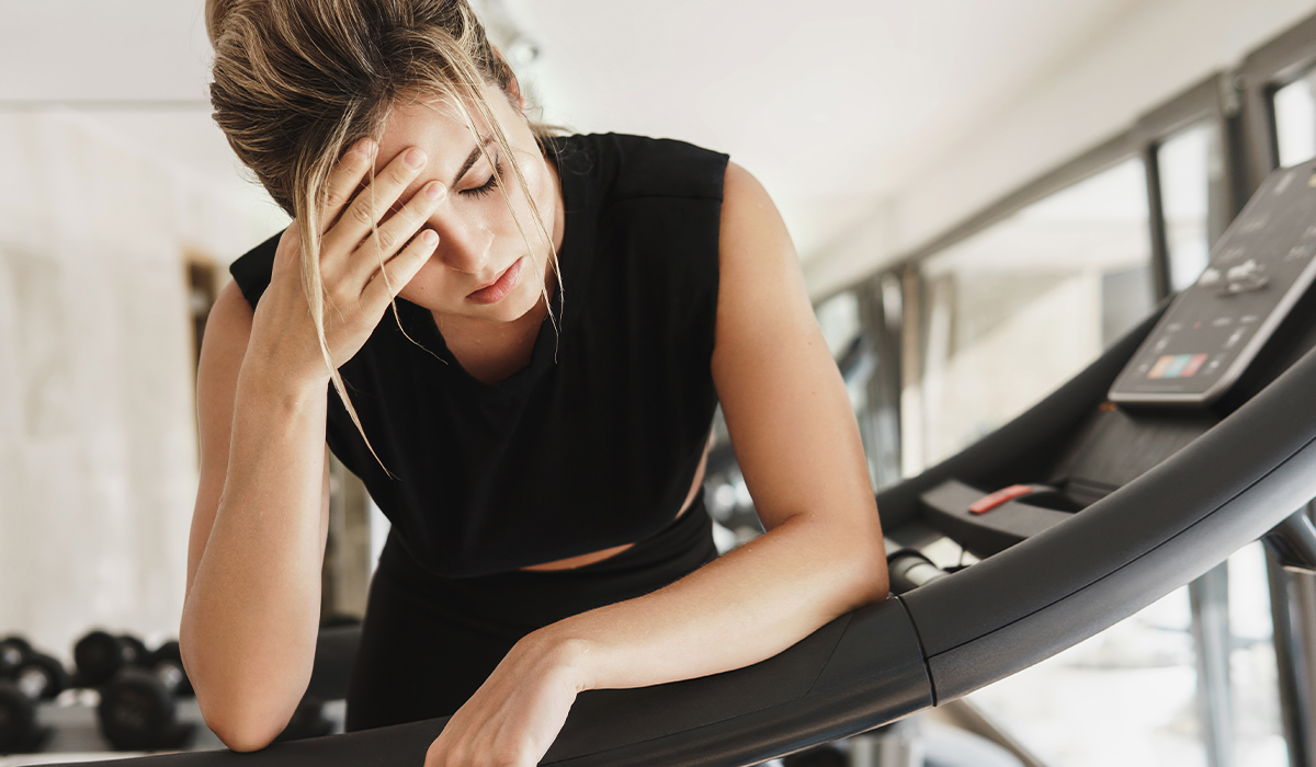 A woman on the treadmill holding her head, exhausted