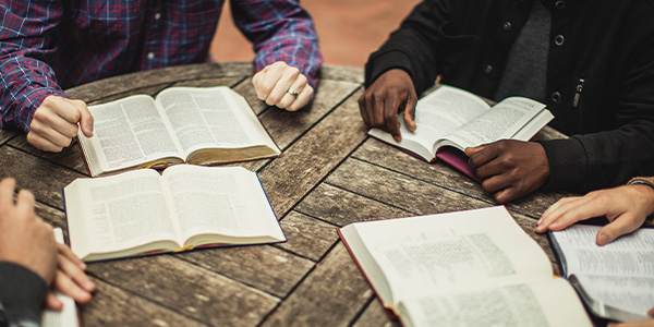 Small group seated around a weathered wooden table with open Bibles in front of them