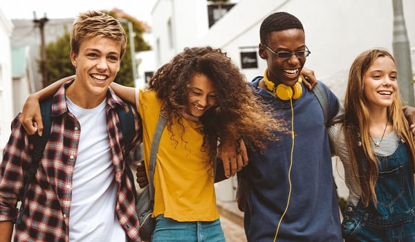 Four smiling teenagers walking arm in arm down a sunny street