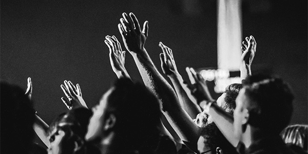 Crowd of people with hands raised in worship at a dimly lit gathering