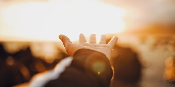 Open hand reaching toward a bright golden sunset