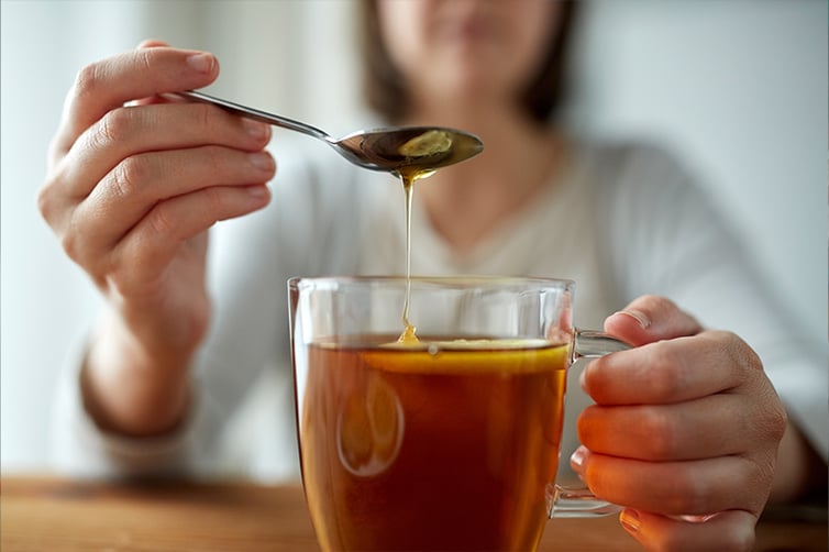 woman adding honey to hot tea