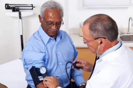 Doctor checking an older man's blood pressure with a cuff and stethoscope in an exam room