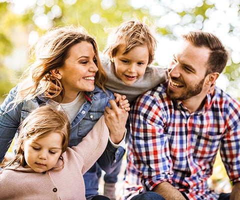 Family of four laughing together outdoors on a sunny day