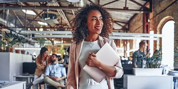 A business woman walking through an office with her laptop