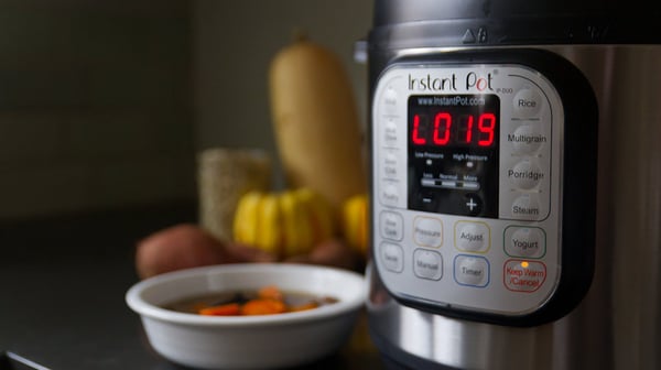 Instant Pot pressure cooker control panel beside a bowl of stew, with squash and sweet potatoes behind