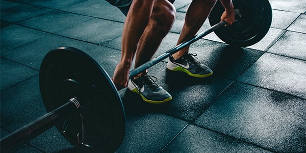 Close-up of a person gripping a loaded barbell on a rubber gym floor, ready to lift