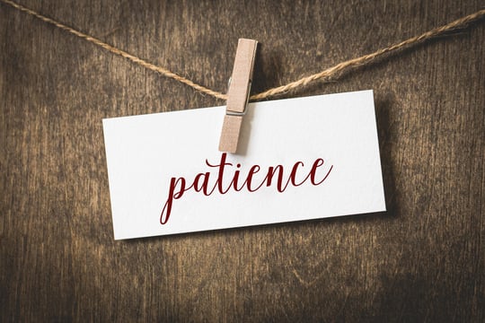 Card with the word patience in red script, clipped with a clothespin to twine against dark wood