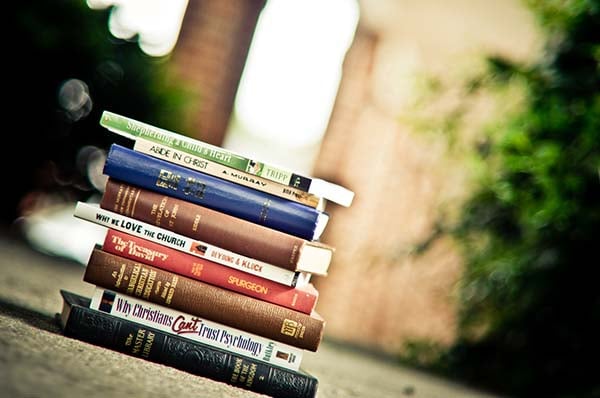 Stack of Christian books, including Abide in Christ and The Treasury of David, on a sidewalk