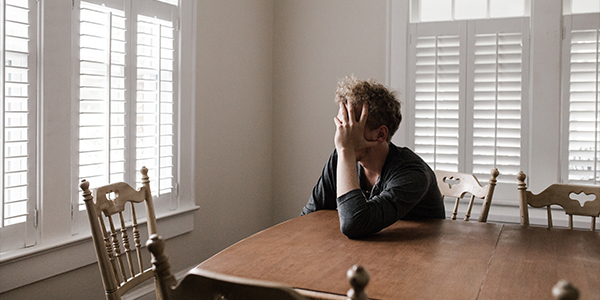 man sitting at kitchen table with head in hands looking frustrated