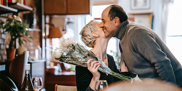 Middle-aged man kissing the cheek of a smiling woman holding a bouquet of white roses