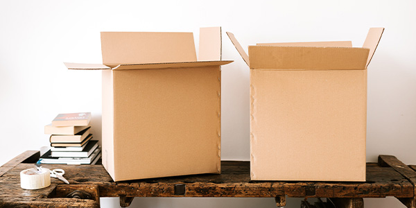Two open cardboard boxes on a rustic wooden table beside a stack of books, packing tape and scissors