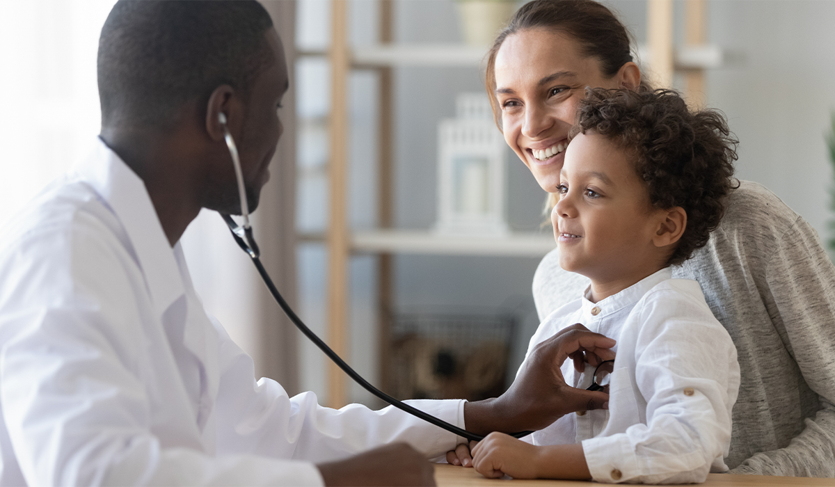 Routine healthcare exam with a stethoscope as a professional listens to a child’s chest while an adult is seated nearby.