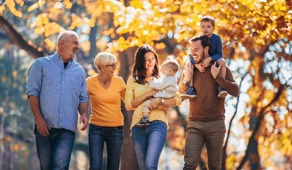 Group of people walking together outside on a tree‑lined path during autumn, with adults carrying young children.