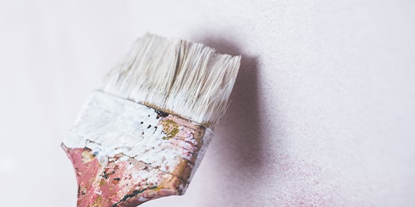 Close-up of a well-used paintbrush with white bristles and a paint-splattered handle against a white wall