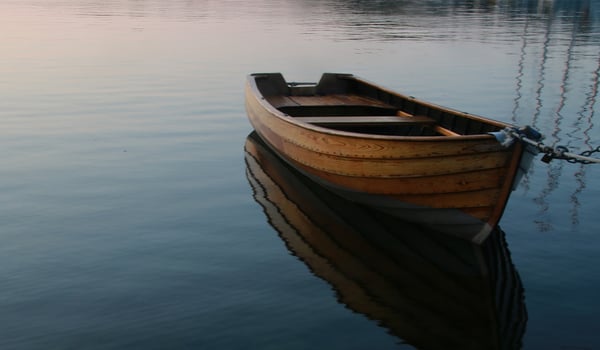 Wooden rowboat moored on calm, still water, its reflection mirrored below