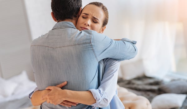 Emotional woman with eyes closed hugs a man in a denim shirt tightly in a bright bedroom