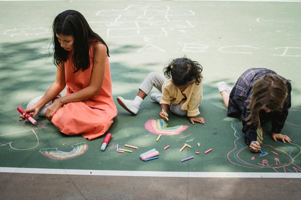 A mom with her two daughters playing with chalk on a sidewalk