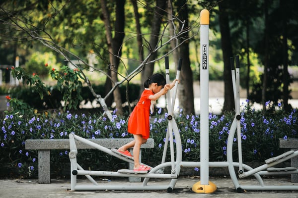 Young girl in a red dress exercising on an outdoor elliptical machine at a park fitness station