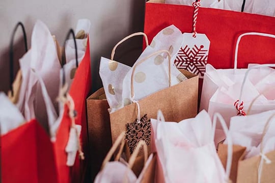 Red, white and kraft paper gift bags filled with tissue paper and decorated with snowflake gift tags