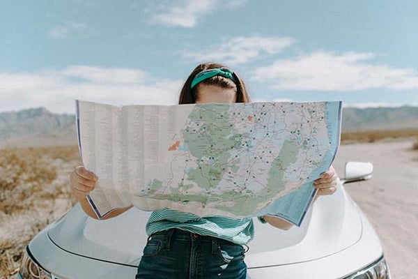 Woman reading a large road map while leaning on the hood of a car on a desert road