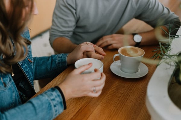 Two people holding hands over cups of coffee at a wooden café table