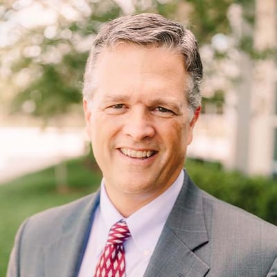 Scott Reddig smiling outdoors in a gray suit and red patterned tie