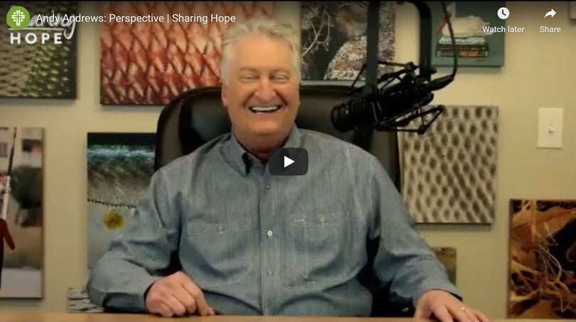 Andy Andrews laughing at a desk beside a studio microphone in a still from the Sharing Hope video Perspective