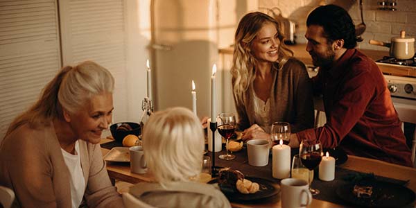 Older woman, young child and two adults laughing together over a candlelit meal at a kitchen table