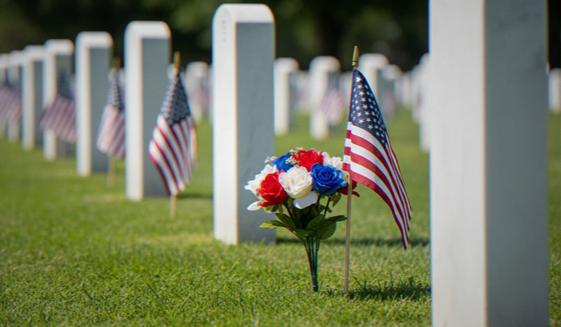 Rows of white headstones decorated with small American flags and a red, white and blue bouquet
