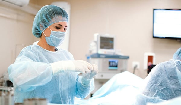 Woman in a surgical cap, mask and gown adjusting sterile gloves in an operating room
