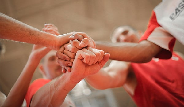 Teammates in red jerseys stack their hands together in a huddle